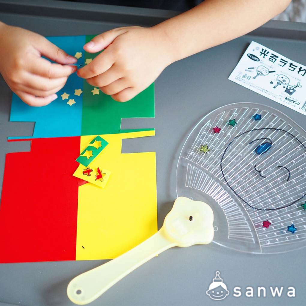 光るうちわにカラーセロハンを貼っている子供の手元