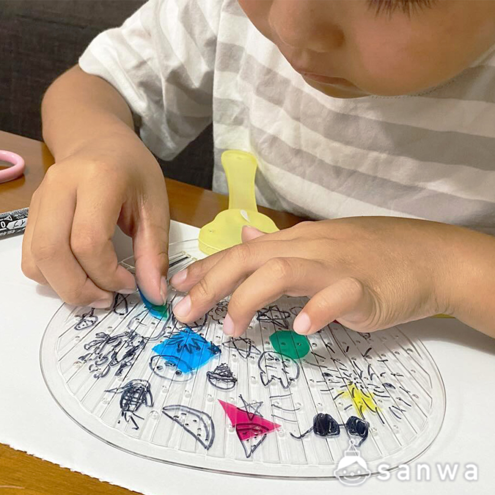 光るうちわにカラーセロハンを貼っている子供の手元